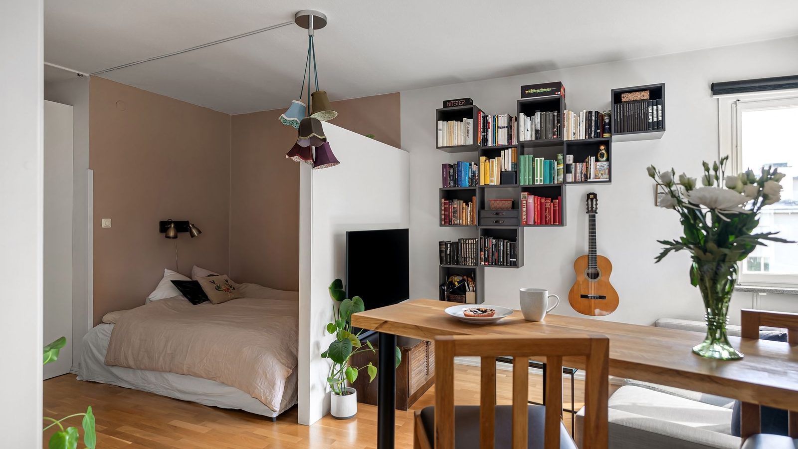 Camera da letto separata dal soggiorno da una parete divisoria, con una libreria a muro e un tavolo di legno